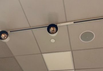 Ceiling with security cameras, LED lights, and HVAC vent in an office space.
